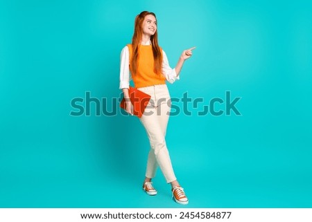 Full length photo of cheerful young woman wear stylish orange clothes hold gadget look empty space isolated on cyan color background