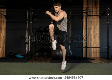 Energetic man doing fitness exercise, warming up and lifting leg, full length shot, gym interior