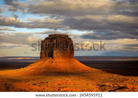 Low rainclouds during sunset hug a butte in Monument Valley's Navajo Tribal Park as rain hydrates the dry desert terrain. Royalty-Free Stock Photo #2454595911