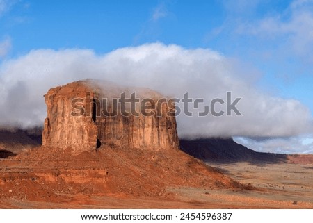 Low rainclouds hug a butte in Monument Valley's Navajo Tribal Park as rain hydrates the dry desert terrain. Royalty-Free Stock Photo #2454596387