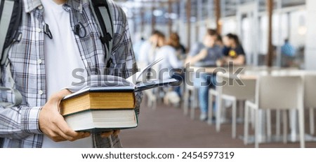 Student holding a stack of textbooks in front of a student cafe. Royalty-Free Stock Photo #2454597319