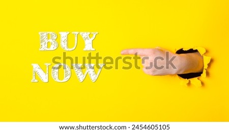 A hand pointing to the word buy now on a yellow background. Concept of urgency or importance, as if the viewer should act quickly to make a purchase