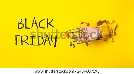 A hand holding a shopping cart with the words Black Friday written in the background. The image has a playful and humorous mood, as it is a creative way to present the holiday shopping season