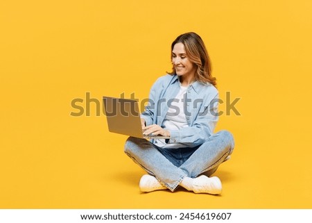Full body smiling happy young IT woman wear blue shirt white t-shirt casual clothes sitting hold use work on laptop pc computer isolated on plain yellow background studio portrait. Lifestyle concept