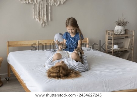 Playful little girl enjoy playtime with loving mother, lying on bed in cozy bedroom, spend carefree pastime at home, tickling each other, laughing feel happy, feel love and attachment. Family leisure Royalty-Free Stock Photo #2454627245