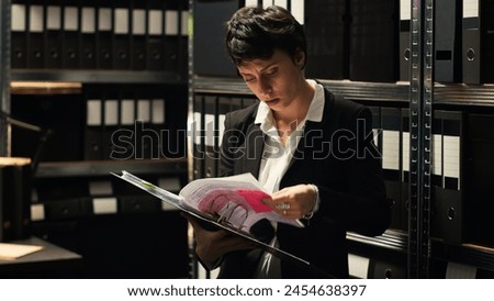Criminal experts finding case clues in confidential record files, conducting investigation to solve crime in incident room. Detectives reading classified documents, secret mission. Handheld shot. Royalty-Free Stock Photo #2454638397