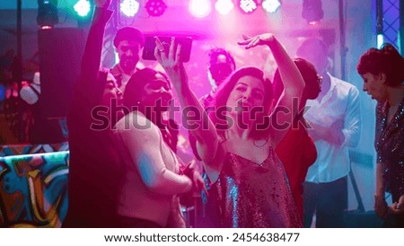 Happy girl taking pictures on phone, recording video for memories to have fun at disco party event. Woman partying with group of friends and taking photos, filming on smartphone. Handheld shot.