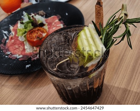 a glass of cold tea with a herbal concoction containing apple slices added with rosemary and cinnamon. Royalty-Free Stock Photo #2454647429