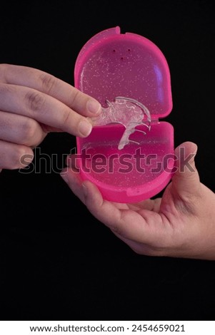 Hands grabbing a Hawley retainer to store it in its case, black background, selective focus, high quality photo, with copy space.