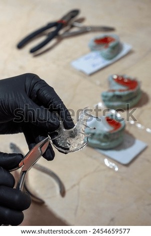 Dental technician working on Hawley retainer on his work table, in the background other completed retainers. selective focus.