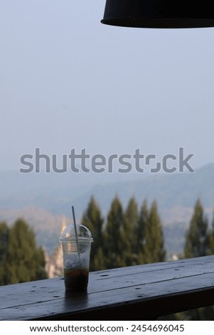 Plastic coffee cups placed on a table in a cafe with mountains and sky in the background.