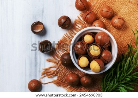 Top view of Dry Roasted Macadamia Nut in white cup on wood background,Macadamia nuts are loaded with flavonoids and tocotrienols and rich in heart-healthy monounsaturated fats Royalty-Free Stock Photo #2454698903