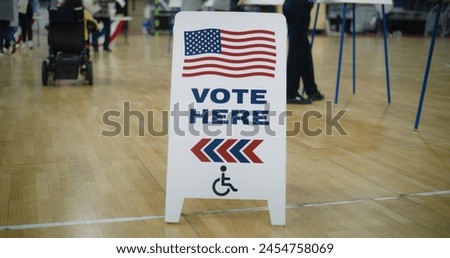 Vote here sign on floor. Woman with spinal muscular atrophy in electric wheelchair comes to vote in polling station. Political races of US presidential candidates. National Election Day. Dolly shot.