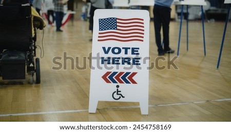 Vote here sign on floor. Woman with spinal muscular atrophy in electric wheelchair comes to vote in polling station. Political races of US presidential candidates. National Election Day. Dolly shot.