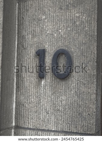 A sign with the number ten on the house. Against the background of a rock wall. uneven texture