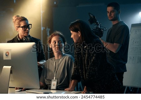 Portrait of video production crew reviewing footage and using computer on set smiling