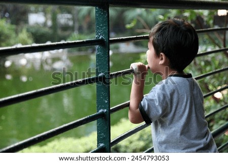 Hong Kong, Asia - 09 03 2011 : Exterior photo portrait view of a curious kid child children asian chinese boy looking over a metal fence grid in a garden botanic park zoo for curiosity about nature 