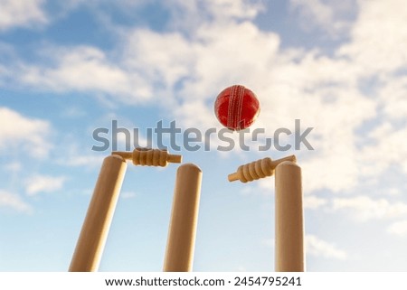 Cricket ball hitting wicket stumps knocking bails out against blue sky background