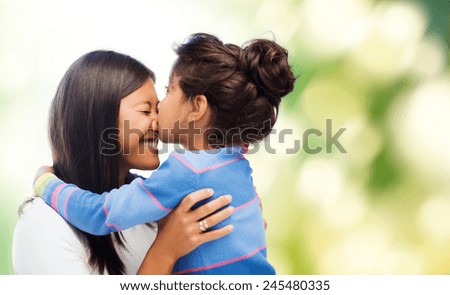 family, children and happy people concept - happy little girl hugging and kissing her mother over green background