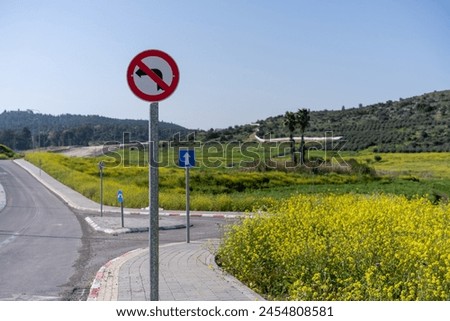 Red and white no left turn traffic sign positioned beside a country road with a beautiful natural landscape. No turning traffic sign with blue one-way arrow against countryside road with yellow blooms