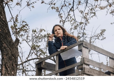 Beautiful pensive girl, inspired dreamy child teenager 8 years old stands on a wooden bridge outdoors in nature, writing poetry and drawing a picture of a landscape. Photography, portrait, lifestyle. Royalty-Free Stock Photo #2454812519