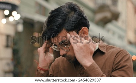 Annoyed angry mad stressed Indian Arabian ethnic male student man guy businessman client customer furious business fail loss dissatisfaction frustration headache touch holding head outside city street Royalty-Free Stock Photo #2454829337