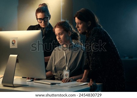 Minimal shot of three women looking at computer screen together on video production set with backlight