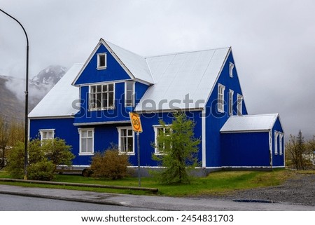 Traditional Icelandic blue residential building with gable roof, white window frames, cladded in corrugated metal sheets in Seydisfjordur town in Iceland with foggy mountains in the background. Royalty-Free Stock Photo #2454831703