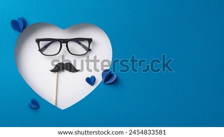 Creative Father's Day concept featuring a white heart with glasses and a mustache prop on a blue background, symbolizing parental love