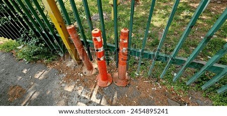 three flexible plastic warning post. plastic parking barrier, red, white and orange anti parking bollard on parking lot in a street with park and nature background. Public parking place