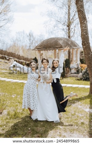 Three women posing for a picture, one of them is wearing a white dress. The other two are wearing black dresses. Scene is happy and celebratory, as the women are posing for a picture together