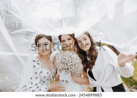 Three women are posing for a photo, with one of them holding a bouquet of flowers. The scene is set in a park, with a white veil covering the women's faces. Scene is lighthearted and joyful