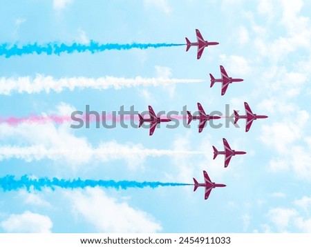 The image shows a formation of nine fighter jets flying in a diamond pattern against a backdrop of a clear blue sky with some scattered clouds. The jets are colored in a combination of red, white, and Royalty-Free Stock Photo #2454911033