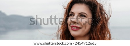 Portrait windswept hair happy woman against a backdrop of mountains and sea. Daylight illuminates the tranquil outdoor setting