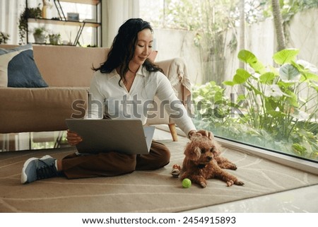 Young woman sitting on floor with opened laptop and petting dog