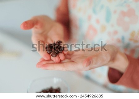 Close-up of girl's hands showing roasted coffee bean with blurred background behind. Shallow depth of field focused on coffee bean. Concept of individual approach to quality control. Royalty-Free Stock Photo #2454926635