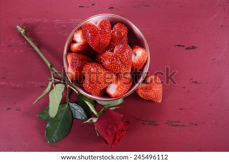 Happy Valentines Day bowl of luscious heart shape red strawberries on a red vintage wood background, with copy space.
