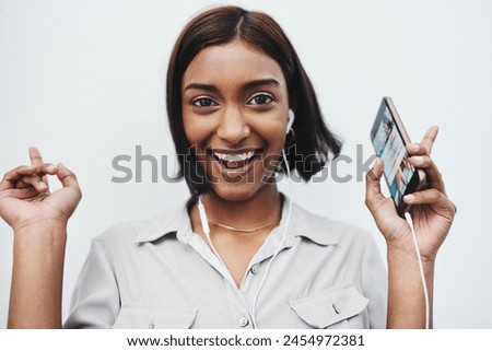 Phone, music and portrait of Indian girl with earphones in studio for dance, track or streaming audio on white background. Smartphone, app or gen z model smile for sign up playlist, radio or podcast