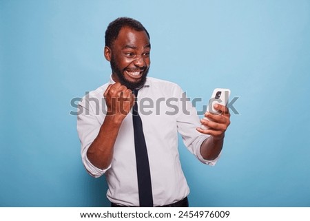 Black man in white shirt holding cellphone winning online mobile game looking tensed at screen. African american gamer testing mobile app on smart phone for the first time feeling enthusiastic.