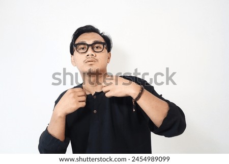 Young Asian man showing arrogant gesture while touching his shirt