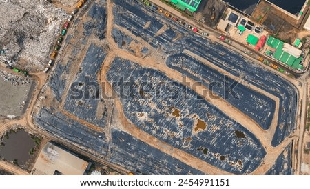 From above, a landfill lies obscured beneath layers of black plastic, a desperate bid to mask our consumption habits. Landfill background. Aerial view.
