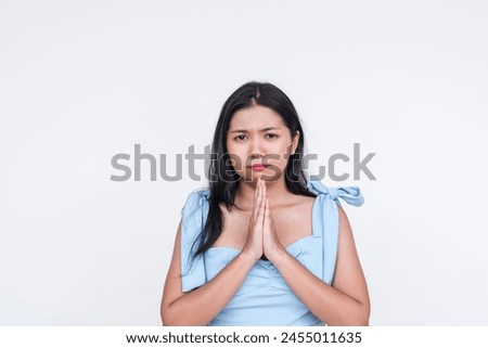 A young Asian woman dressed in a light blue dress pouts charmingly while pleading for a favor, set against a clean white background.
