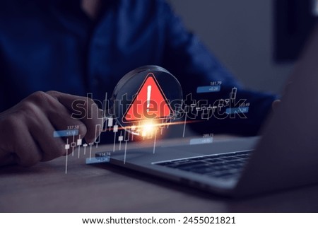 Businessman uses laptop with virtual warning sign to caution in investing, warning of economic situation, investment risk.
