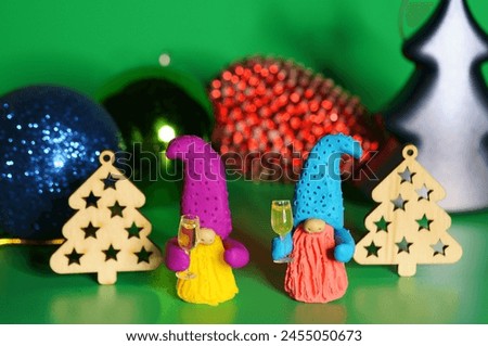 Two toy dwarfs made of plasticine with glasses of champagne on the background of Christmas decorations. New Year's holidays and Christmas. Decorations and decorations. Green background.
