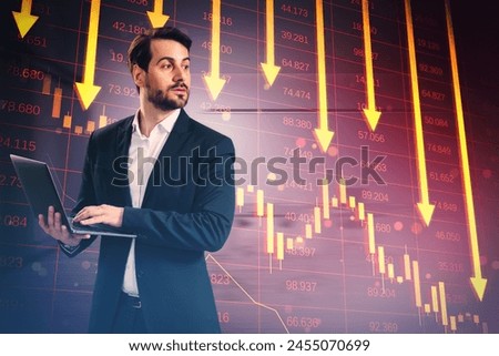 Worried young european businessman with laptop and red crisis arrows on blurry background. Economic recession, financial fall and crash concept. Double exposure