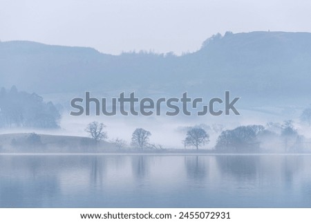 Stunning peaceful landscape image of misty Spring morning over Windermere in Lake District with boats moored on lake and distant misty peaks