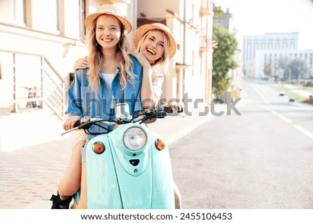 Two young beautiful smiling hipster female in trendy clothes. Carefree women driving retro motorbike on the street background. Positive models having fun, riding classic Italian scooter in Europe city