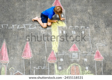 Little kid boy drawing knight castle and fortress with colorful chalks. Happy preschool child having fun with creating chalk picture. Creative leisure for kids and children in summer
