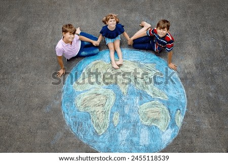 Little preschool girl and two school kids boys with earth globe painting with colorful chalks on ground. Happy earth day concept. Creation of children for saving world, environment and ecology.