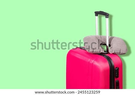 Pink suitcase and gray travel pillow on a green background. Travel concept. Free space for text.